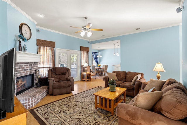 living room featuring french doors, ceiling fan, ornamental molding, light wood-type flooring, and a brick fireplace