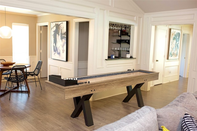 game room with hardwood / wood-style flooring, ornamental molding, vaulted ceiling, and bar area