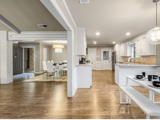 kitchen featuring hanging light fixtures, light stone countertops, crown molding, hardwood / wood-style floors, and white cabinetry