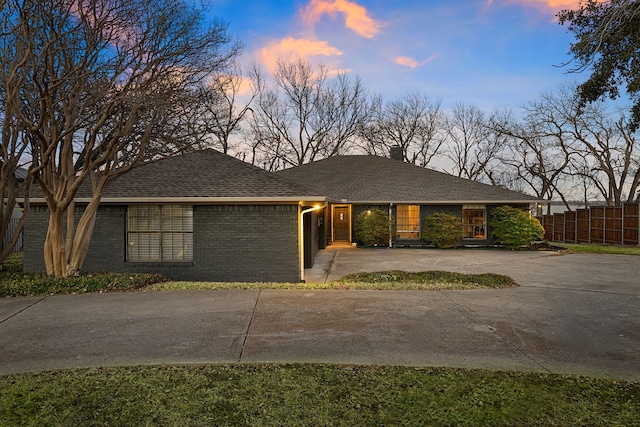 view of front of house with a shingled roof, brick siding, and fence