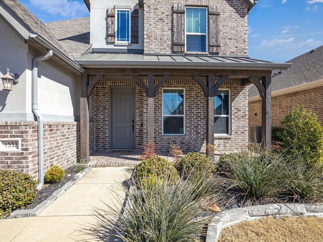 view of exterior entry featuring a standing seam roof, metal roof, stucco siding, and brick siding