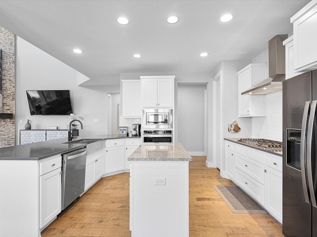 kitchen featuring stainless steel appliances, light wood-style flooring, white cabinetry, a kitchen island, and wall chimney exhaust hood