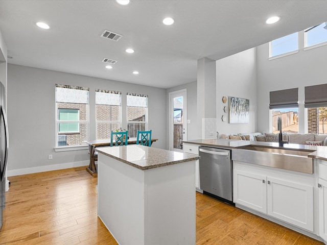 kitchen with a sink, white cabinetry, open floor plan, a center island, and dishwasher