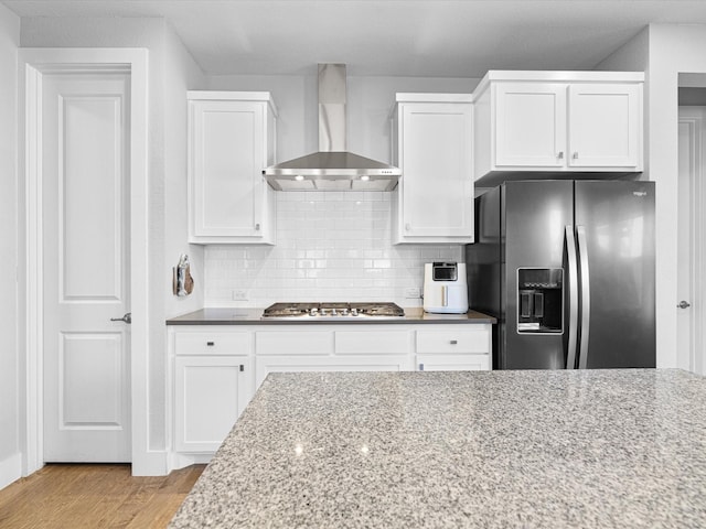 kitchen featuring white cabinets, wall chimney range hood, light stone counters, and stainless steel appliances