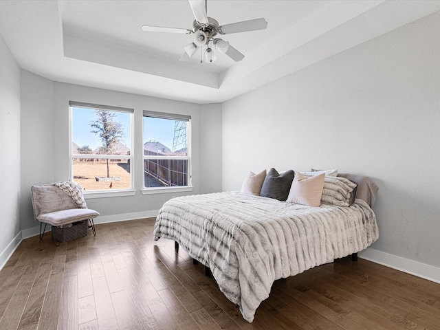 bedroom featuring ceiling fan, baseboards, a tray ceiling, and dark wood finished floors