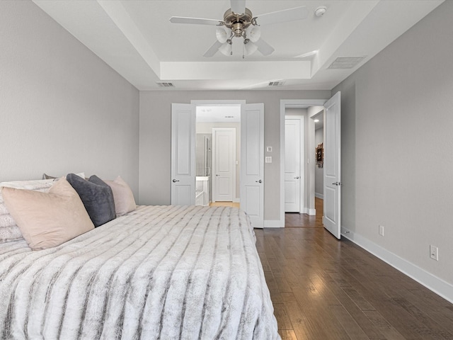 bedroom featuring a tray ceiling, dark wood-style flooring, visible vents, and baseboards