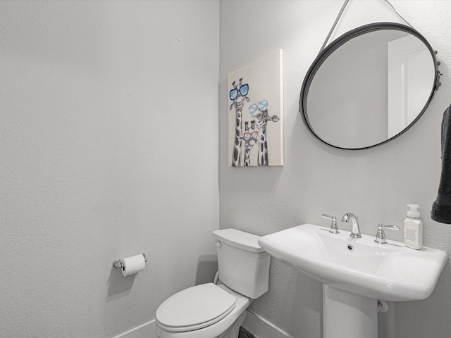 bathroom featuring a textured wall, a sink, toilet, and baseboards