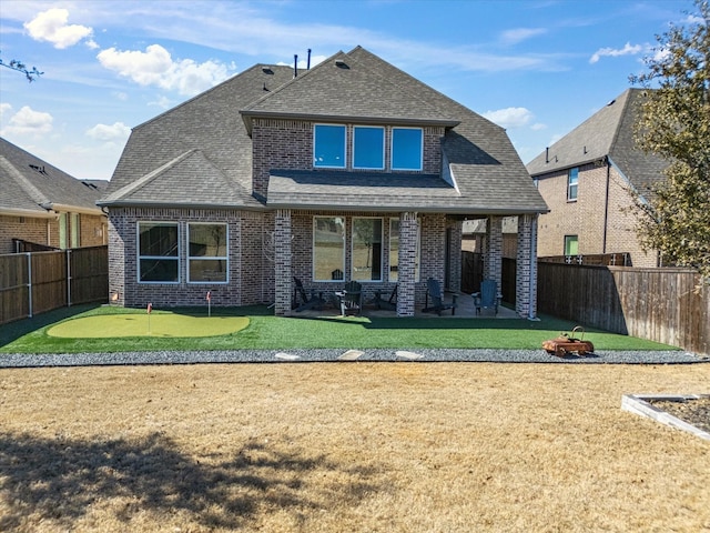 back of property featuring a shingled roof, a fenced backyard, and brick siding