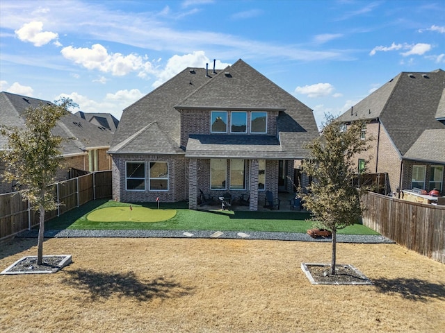 back of property featuring brick siding, roof with shingles, a lawn, a residential view, and a fenced backyard