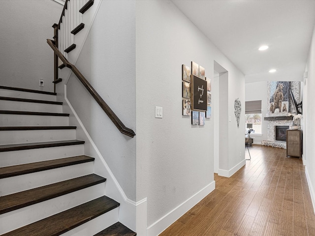 staircase featuring recessed lighting, wood-type flooring, baseboards, and a glass covered fireplace