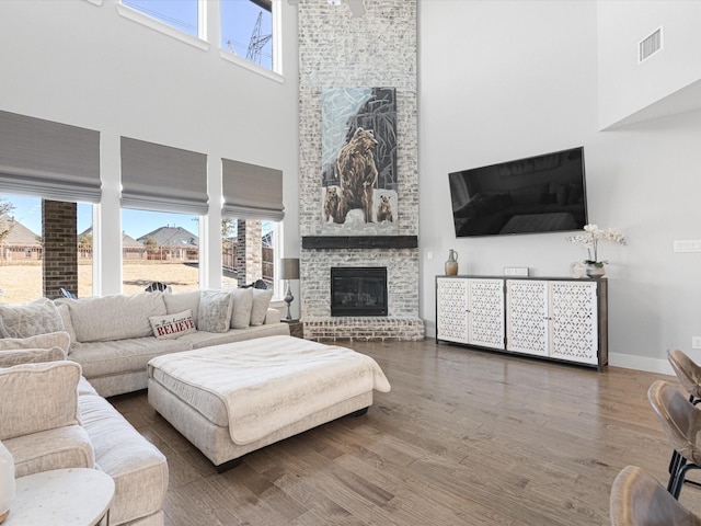 living room with a brick fireplace, dark wood finished floors, visible vents, and a healthy amount of sunlight