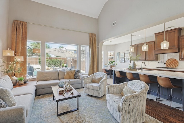 living room with arched walkways, high vaulted ceiling, wood finished floors, and visible vents