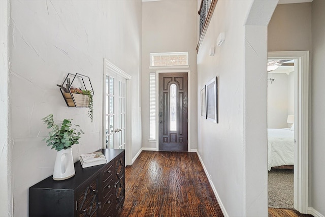 entryway with dark wood-type flooring, a high ceiling, and baseboards