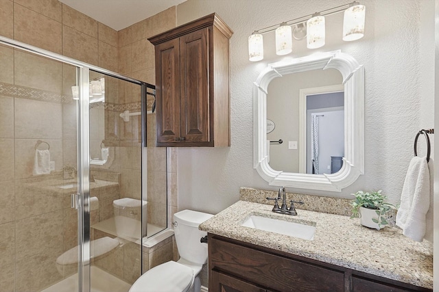 full bath featuring a stall shower, a textured wall, vanity, and toilet