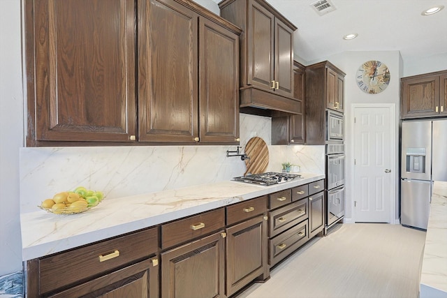 kitchen featuring visible vents, light stone counters, appliances with stainless steel finishes, dark brown cabinets, and premium range hood