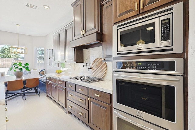 kitchen featuring stainless steel appliances, dark brown cabinets, light stone counters, and decorative backsplash