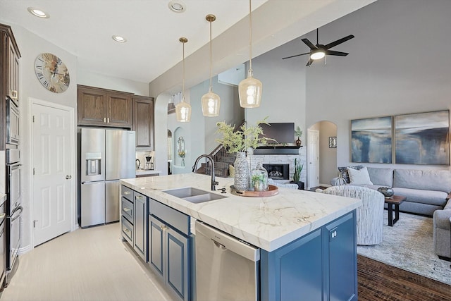 kitchen with arched walkways, a sink, open floor plan, appliances with stainless steel finishes, and an island with sink