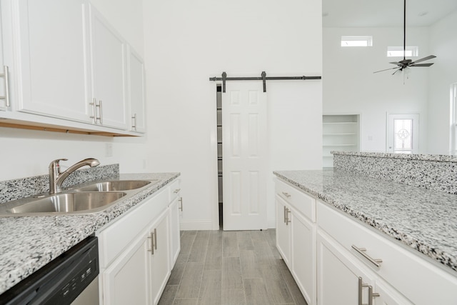 kitchen with light stone counters, a barn door, white cabinets, a sink, and dishwasher