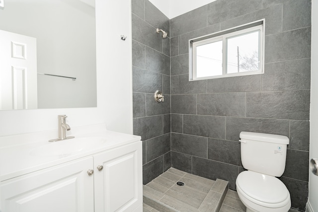 bathroom with toilet, a tile shower, and vanity