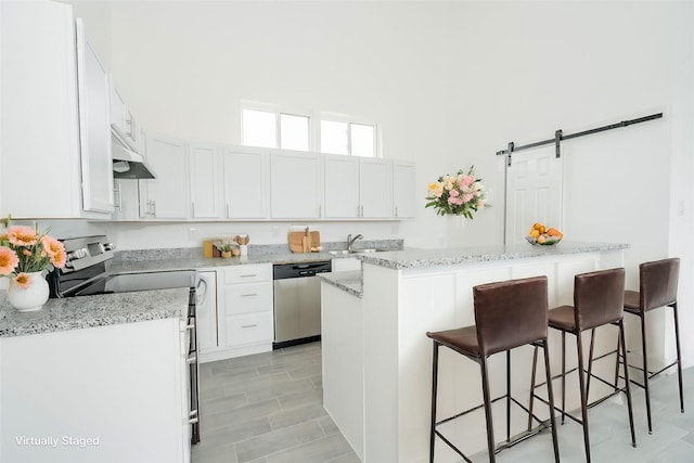 kitchen with a barn door, a breakfast bar area, a center island, stainless steel appliances, and white cabinetry