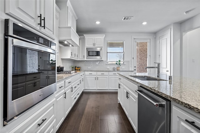 kitchen with light stone counters, appliances with stainless steel finishes, white cabinets, and a sink