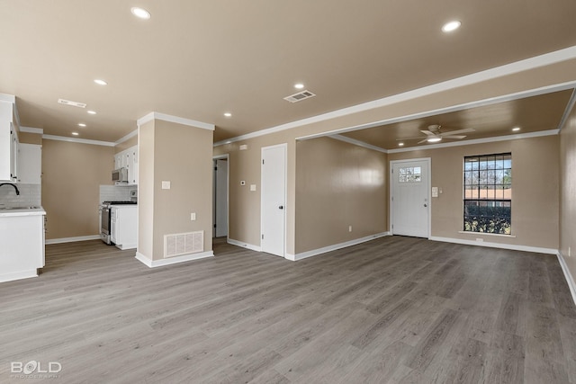 unfurnished living room featuring light wood-type flooring, sink, ornamental molding, and ceiling fan