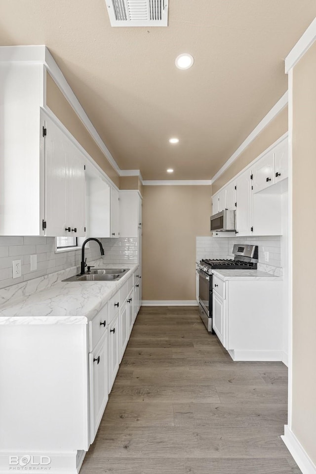 kitchen featuring light hardwood / wood-style floors, sink, ornamental molding, appliances with stainless steel finishes, and white cabinets