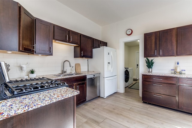 kitchen featuring light stone counters, white refrigerator with ice dispenser, a sink, stainless steel dishwasher, and washer / dryer