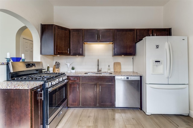 kitchen with a sink, light wood-style floors, appliances with stainless steel finishes, backsplash, and light stone countertops