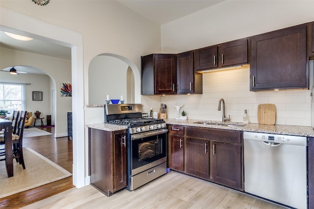 kitchen with light stone countertops, appliances with stainless steel finishes, dark brown cabinets, and a sink