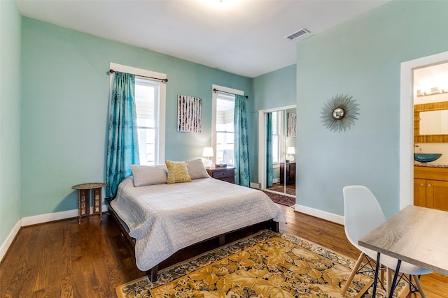 bedroom featuring dark wood-style floors, ensuite bath, visible vents, and baseboards