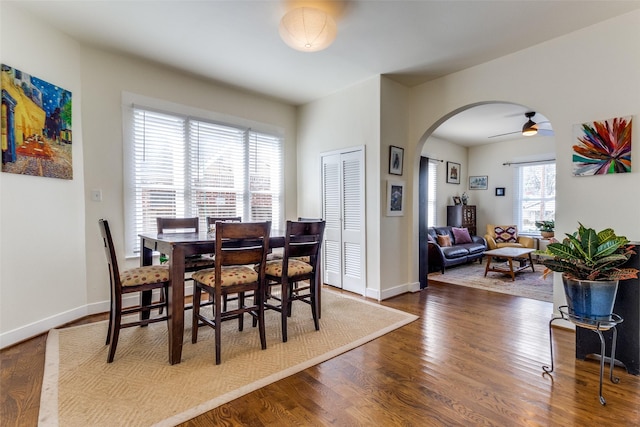 dining area with baseboards, arched walkways, dark wood finished floors, and a ceiling fan