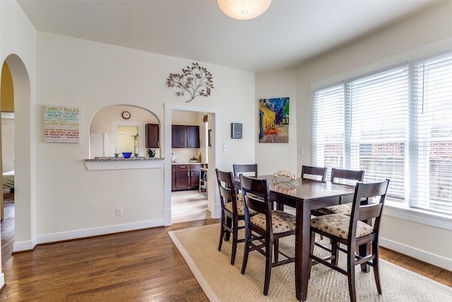 dining room with arched walkways, dark wood-type flooring, and baseboards