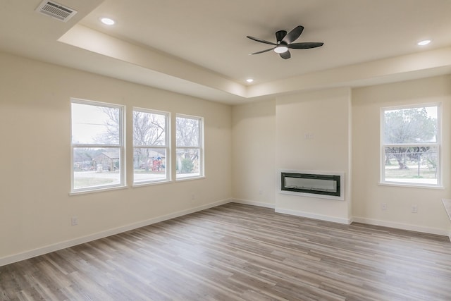 unfurnished living room featuring ceiling fan, light hardwood / wood-style flooring, and a raised ceiling