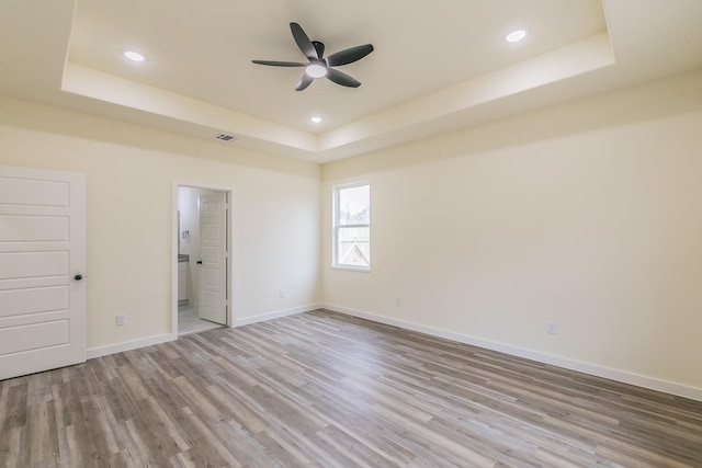 unfurnished bedroom featuring a tray ceiling, ceiling fan, wood-type flooring, and ensuite bathroom