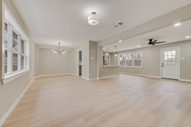 unfurnished living room with ceiling fan with notable chandelier and light hardwood / wood-style flooring