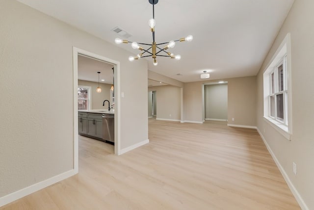 empty room with sink, a notable chandelier, and light hardwood / wood-style flooring