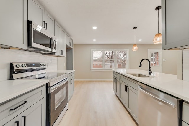 kitchen featuring gray cabinetry, hanging light fixtures, sink, backsplash, and appliances with stainless steel finishes