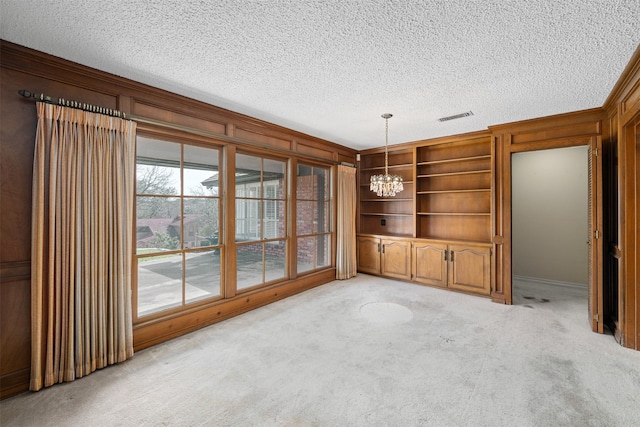 unfurnished living room with light carpet, a chandelier, wood walls, and a textured ceiling