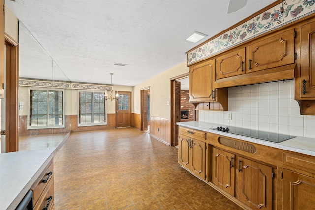 kitchen featuring an inviting chandelier, a textured ceiling, decorative light fixtures, black electric stovetop, and decorative backsplash