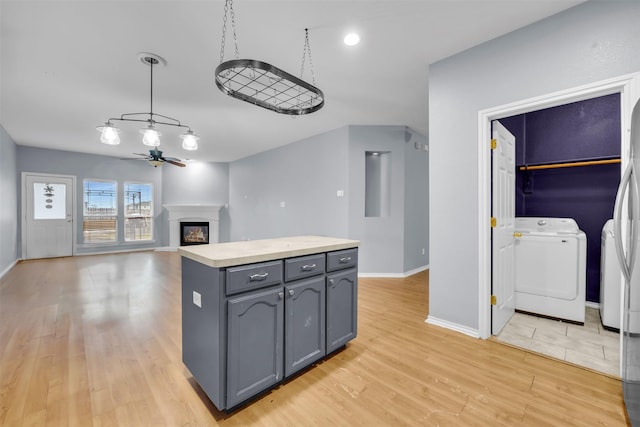 kitchen featuring light hardwood / wood-style flooring, a center island, separate washer and dryer, decorative light fixtures, and ceiling fan