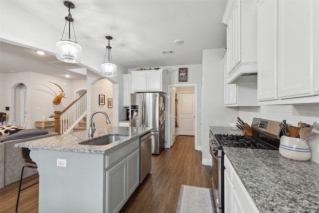 kitchen with sink, light stone counters, white cabinetry, stainless steel appliances, and an island with sink