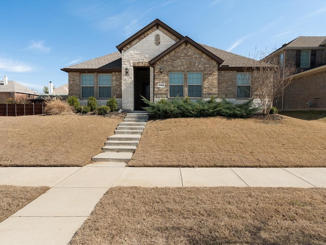 view of front of house with stone siding, roof with shingles, a front yard, and brick siding