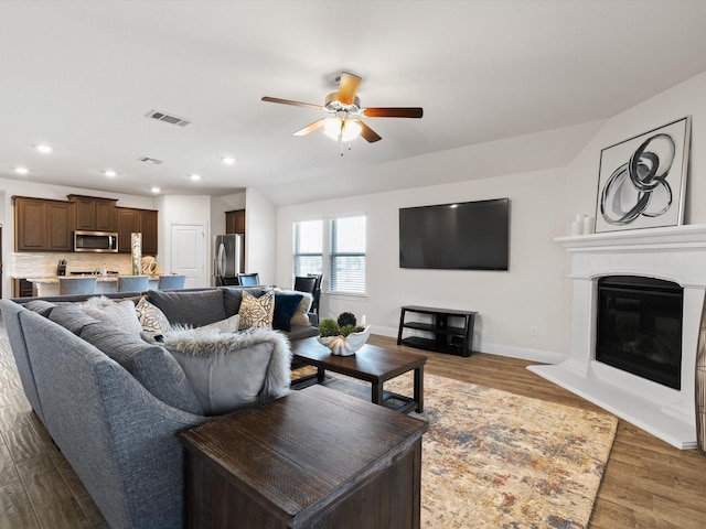 living room featuring baseboards, visible vents, dark wood-type flooring, and a glass covered fireplace