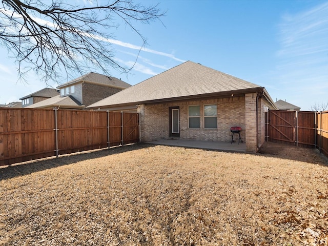 back of property with brick siding, a shingled roof, a gate, a patio area, and a fenced backyard