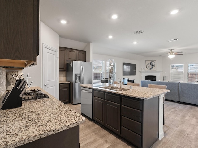 kitchen with visible vents, an island with sink, open floor plan, stainless steel appliances, and a fireplace