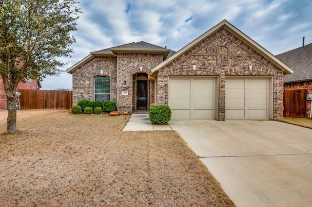 french country style house featuring an attached garage, concrete driveway, fence, and brick siding