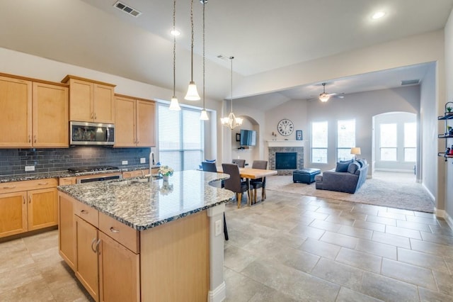 kitchen featuring visible vents, a center island with sink, appliances with stainless steel finishes, arched walkways, and open floor plan