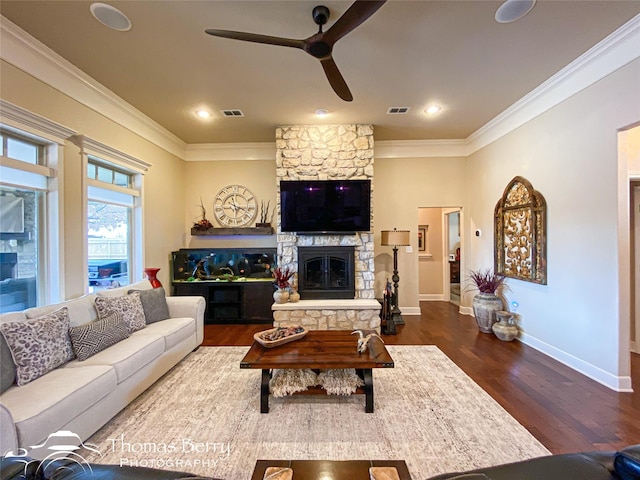 living area featuring ornamental molding, a stone fireplace, dark wood finished floors, and visible vents