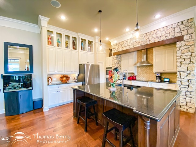 kitchen featuring a spacious island, white cabinetry, freestanding refrigerator, wall chimney exhaust hood, and glass insert cabinets